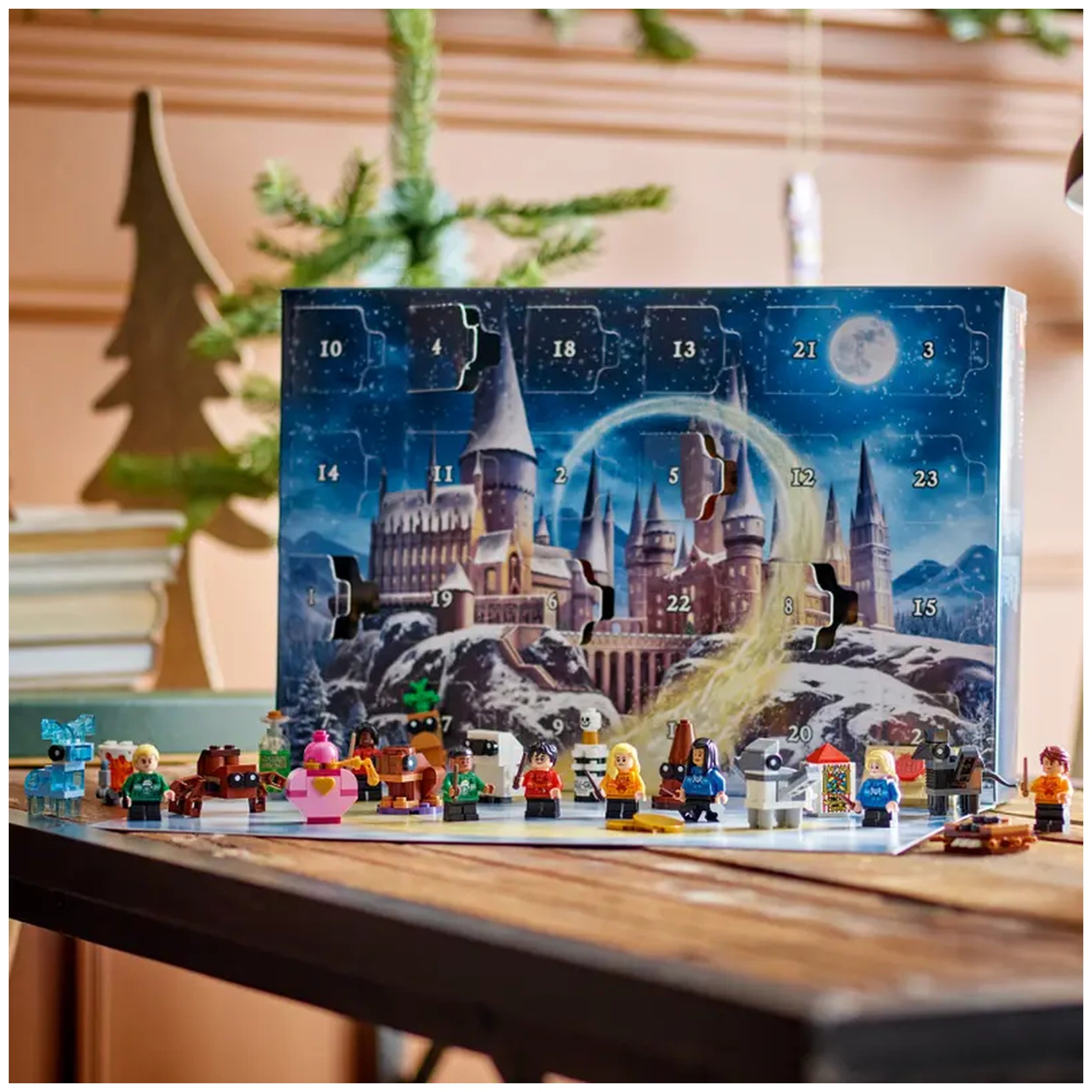 LEGO Harry Potter Advent Calendar 2025 displayed on a wooden table, featuring a colorful castle backdrop and 14 buildable minifigures in festive attire, including iconic characters, along with magical creatures.