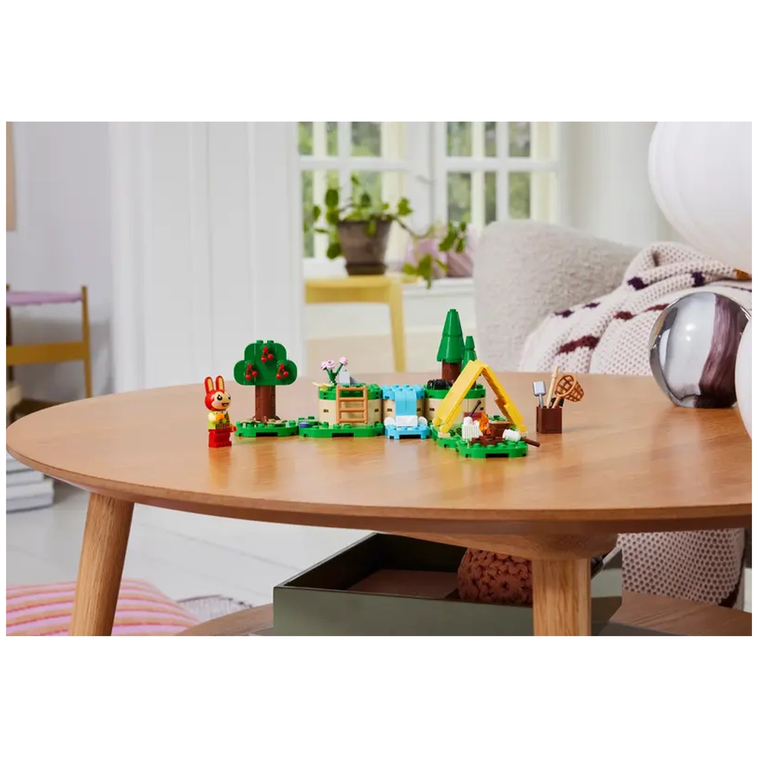Colorful LEGO® Animal Crossing™ Bunnie's Outdoor Activities set featuring a tent, tree, creek, and accessories on a wooden table.