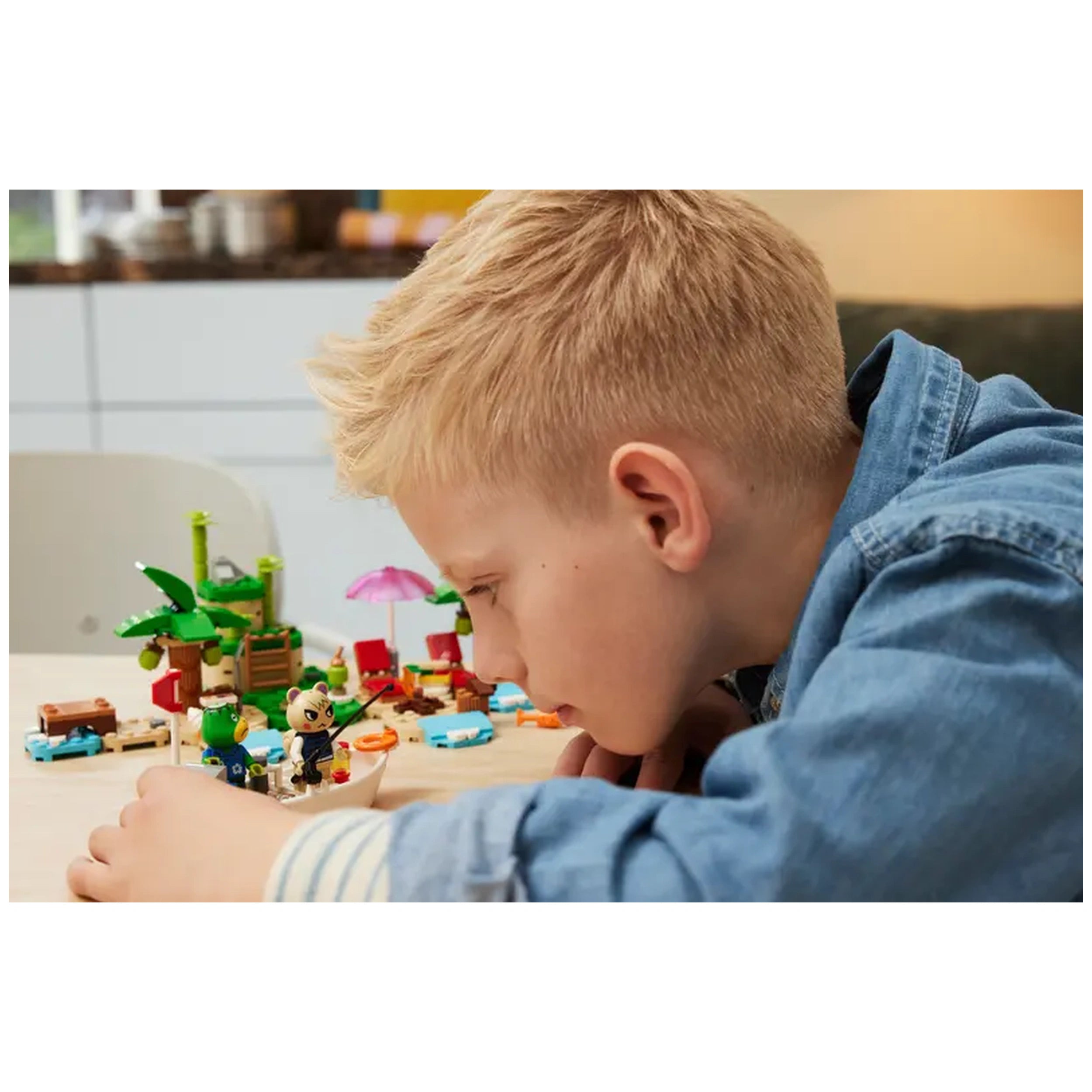 A child intently builds with the LEGO® Animal Crossing™ Kapp’n’s Island Boat Tour set, featuring vibrant pieces like palm trees and a boat.