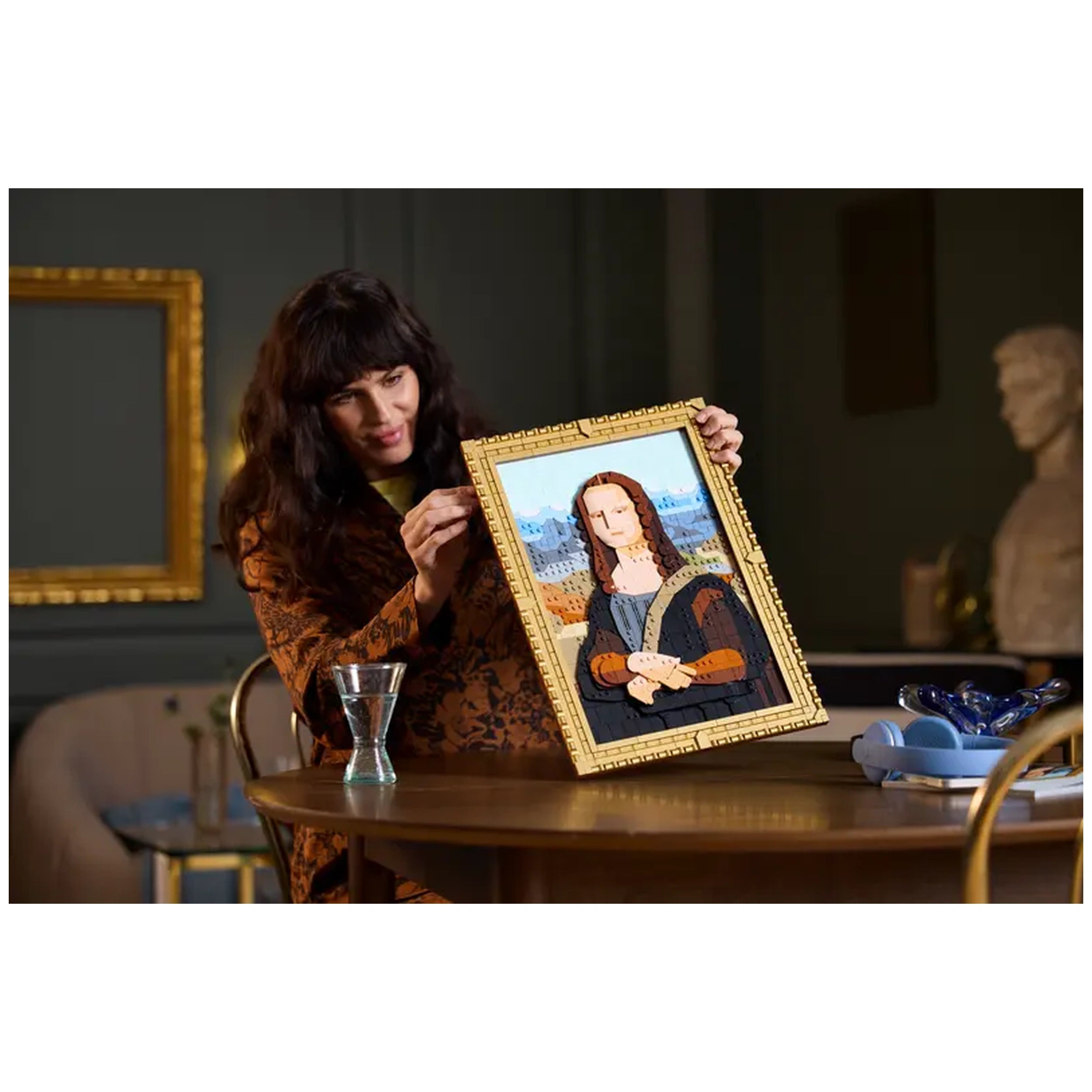 A woman admires a LEGO® Art Mona Lisa set, displaying an intricately built version of the iconic painting in a golden frame, on a table.