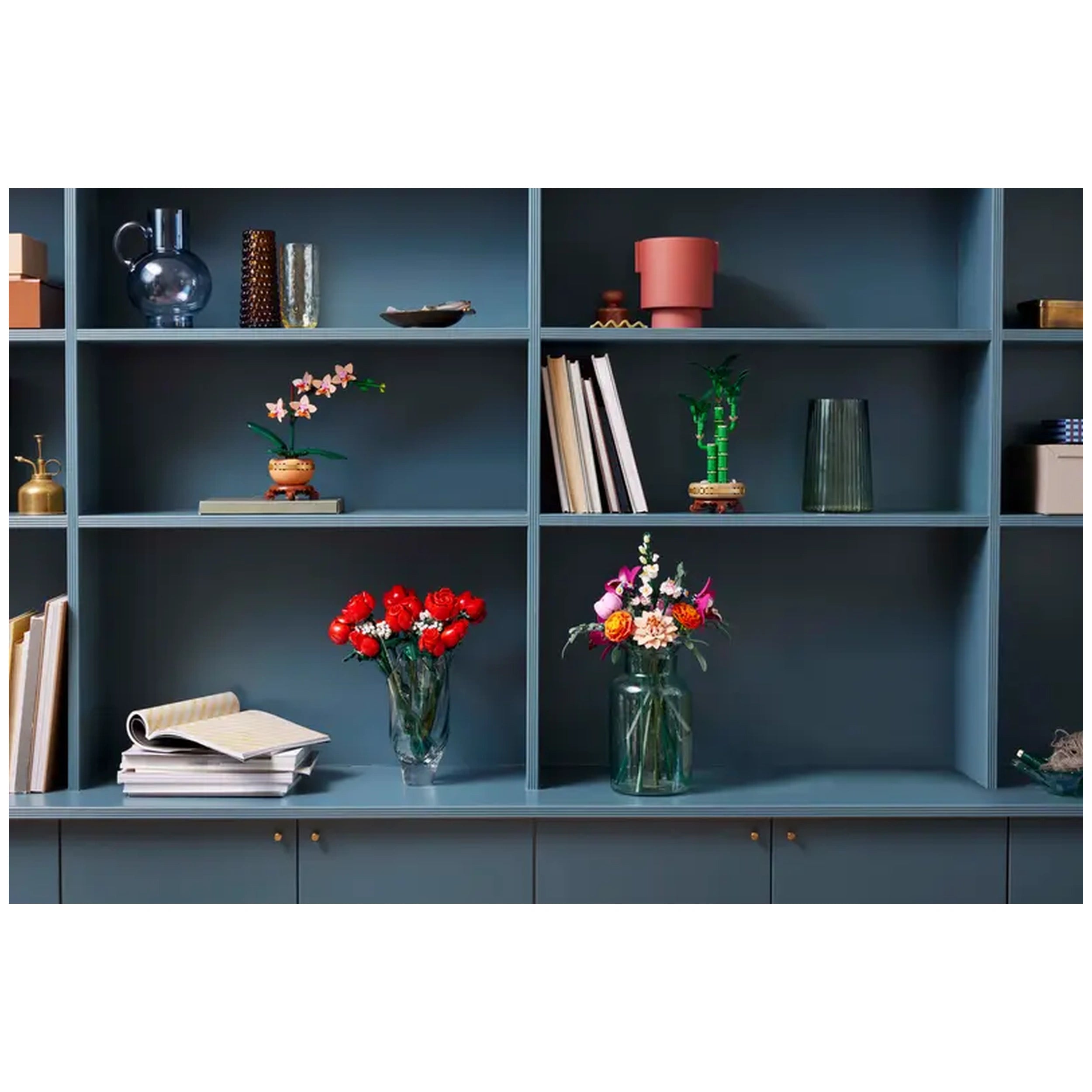 Colorful arrangement of flowers, including a vase of red roses and a jar with mixed blooms, displayed on a blue shelf.