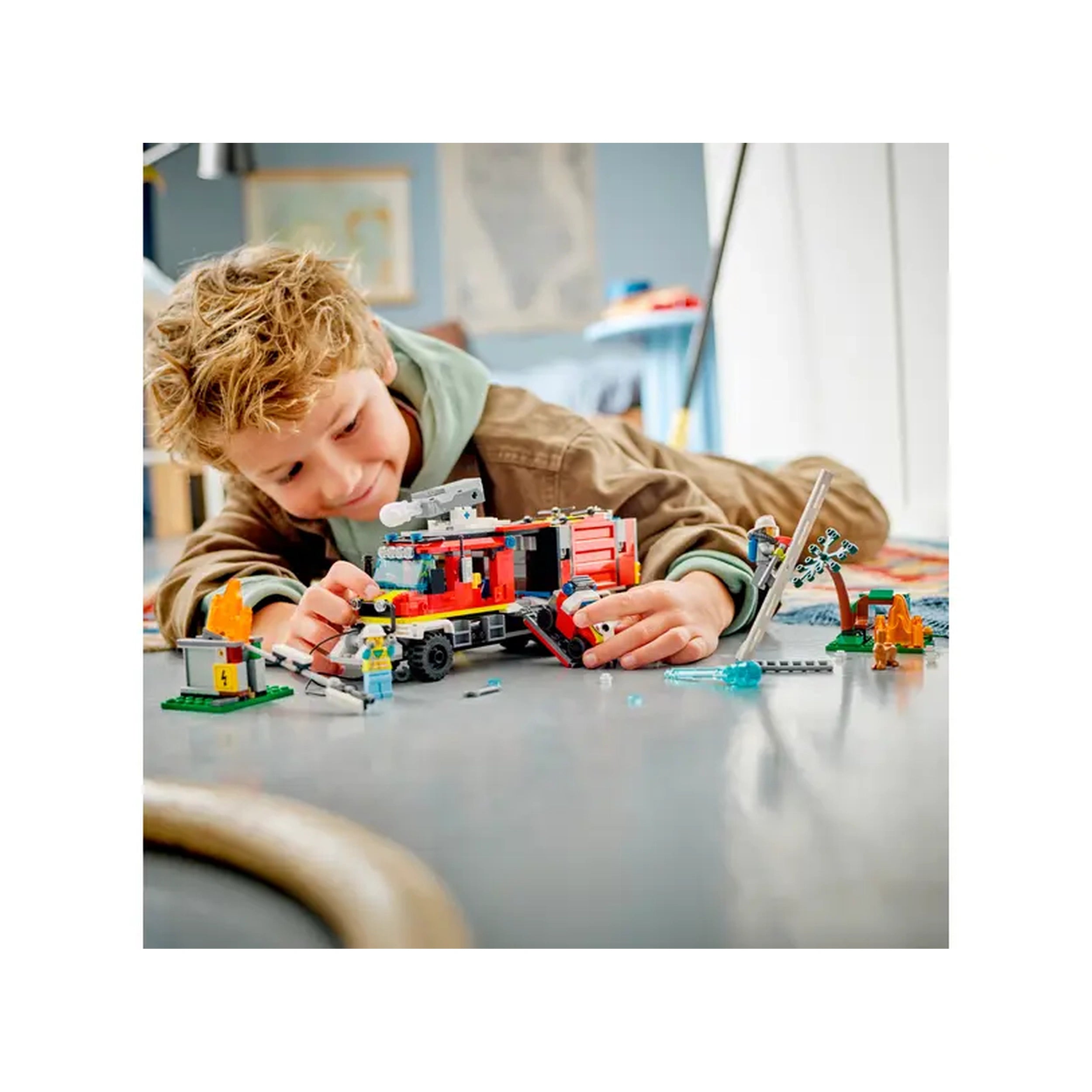 A child enthusiastically plays with the LEGO City Fire Command Truck set, surrounded by firefighting accessories and minifigures on a bright floor.