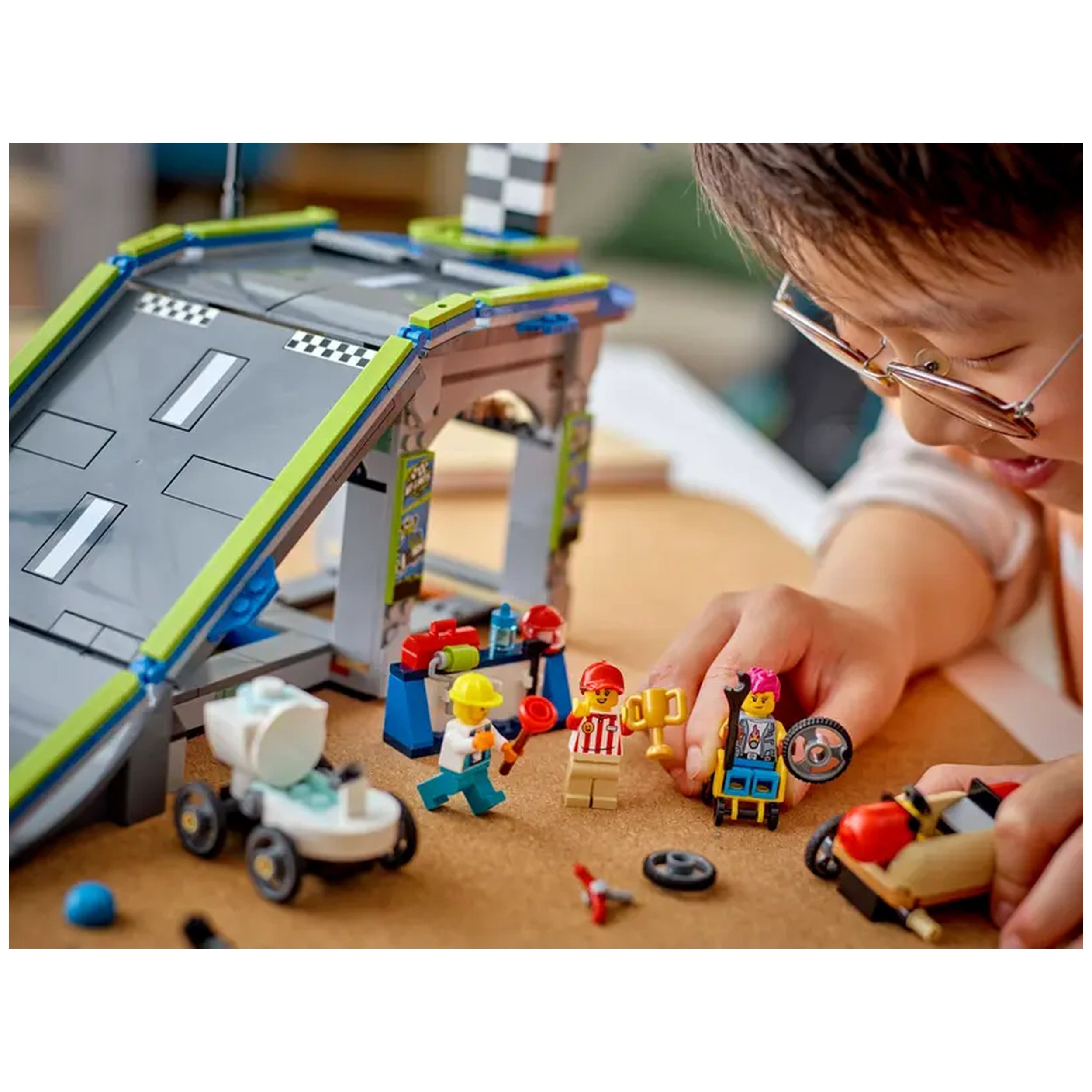 A child plays with the LEGO City Race Car Ramp Track set, featuring a tall ramp and colorful mini figures celebrating a race.