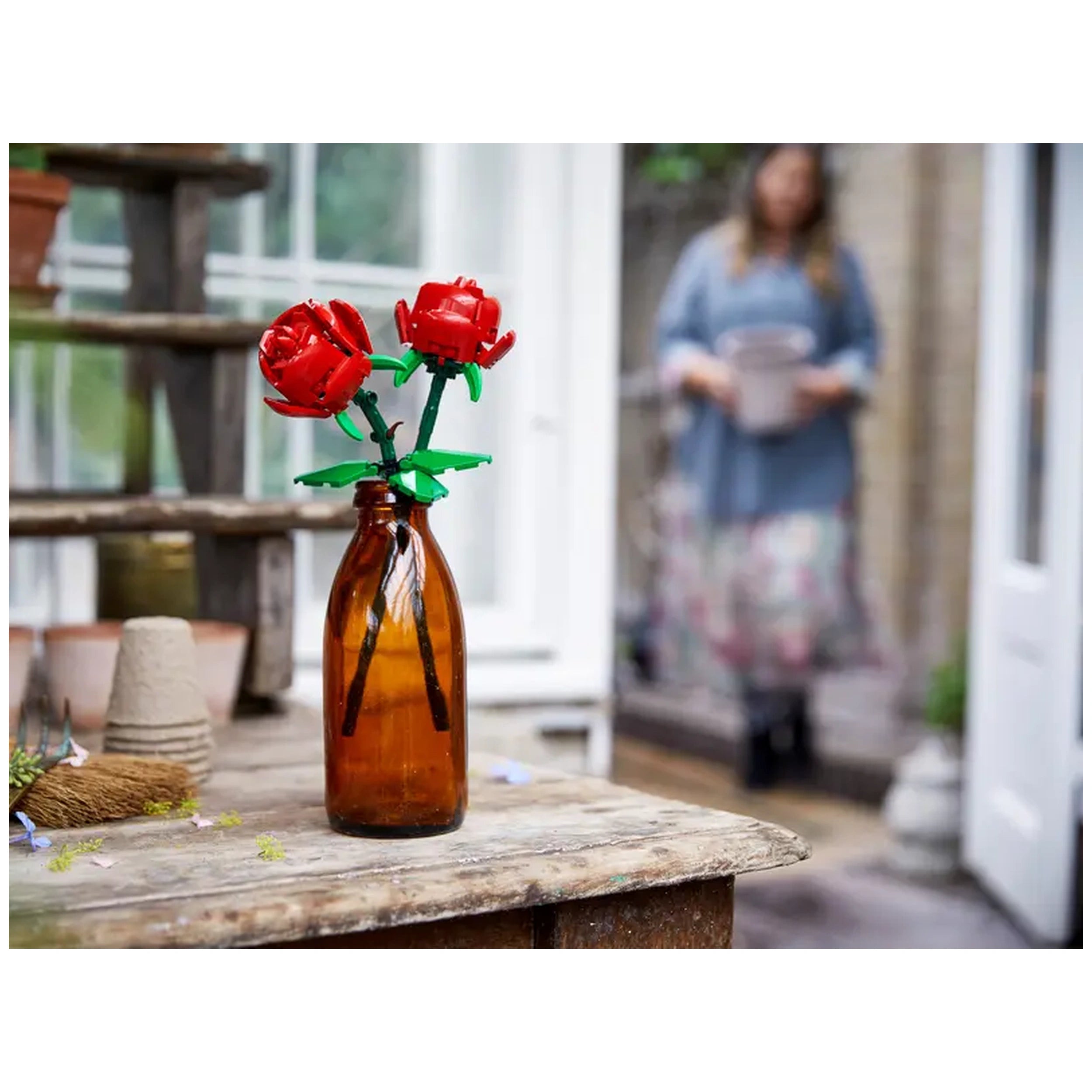 LEGO® Creator Botanical - Roses set in an amber bottle, featuring two vibrant red roses with green leaves, on a rustic wooden table.