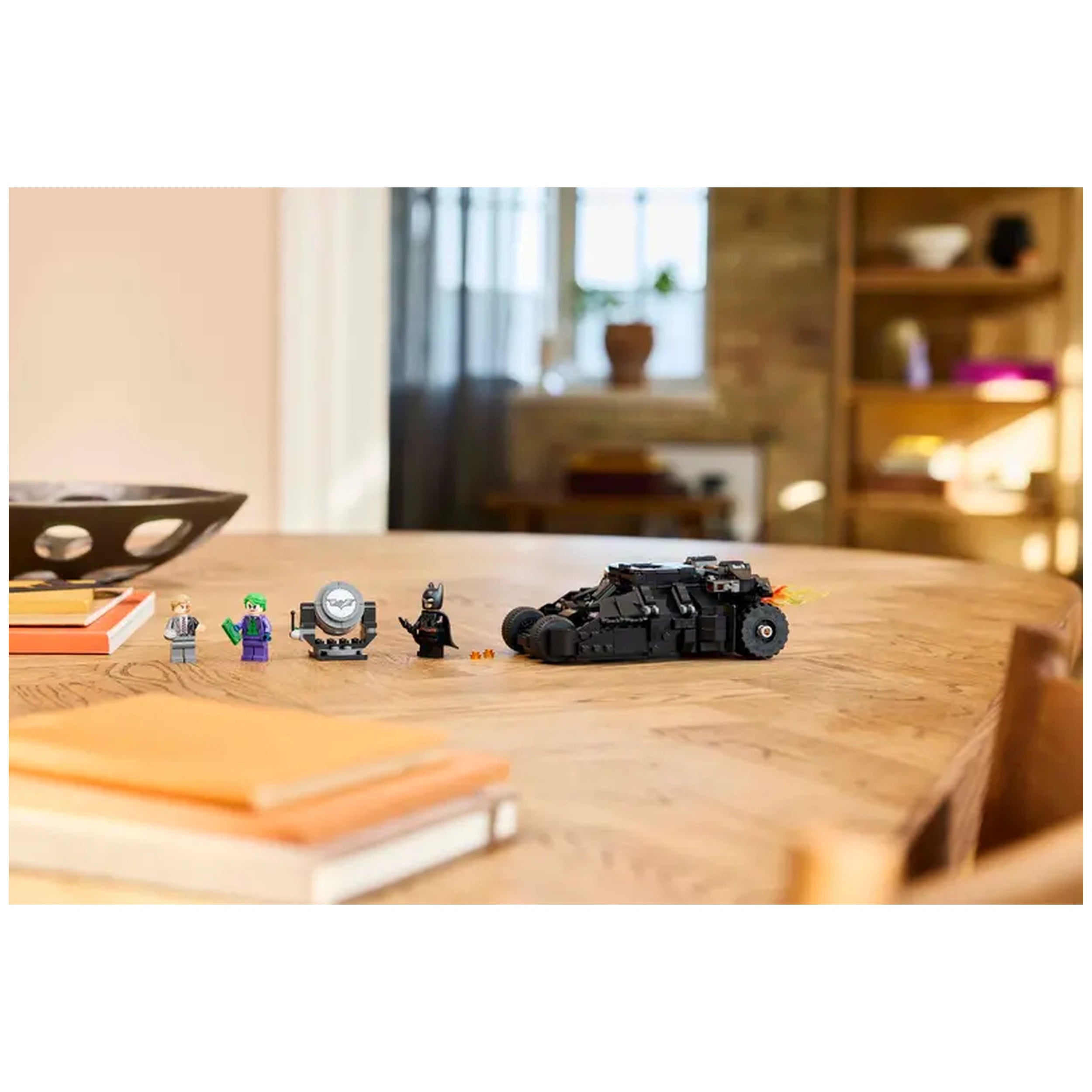 LEGO Batman Tumbler with Two-Face and Joker minifigures, displayed on a wooden table with orange notebooks in a bright room.