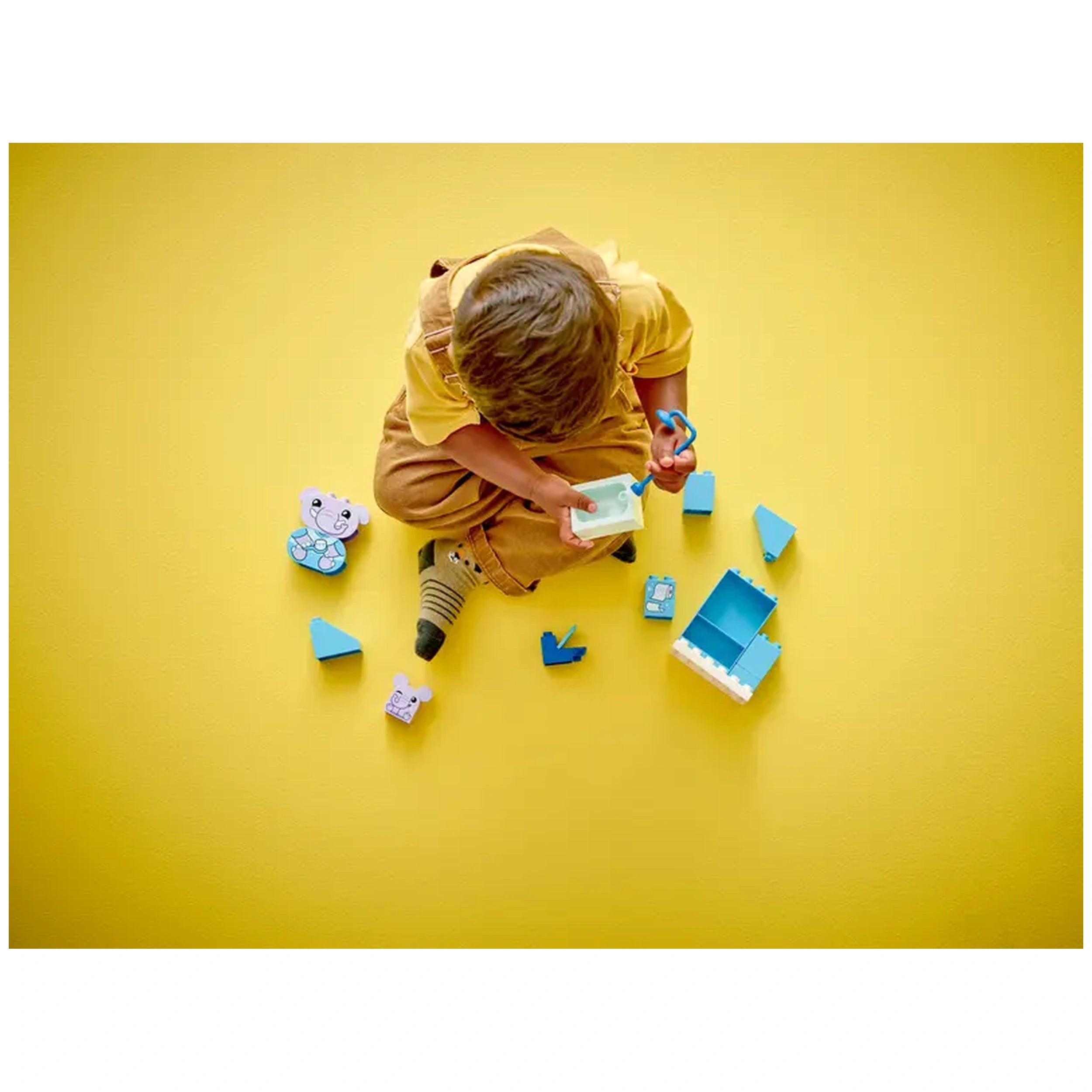 Child sitting on a yellow floor, playing with LEGO® DUPLO® Bath Time set pieces, including a blue box and animal figures.