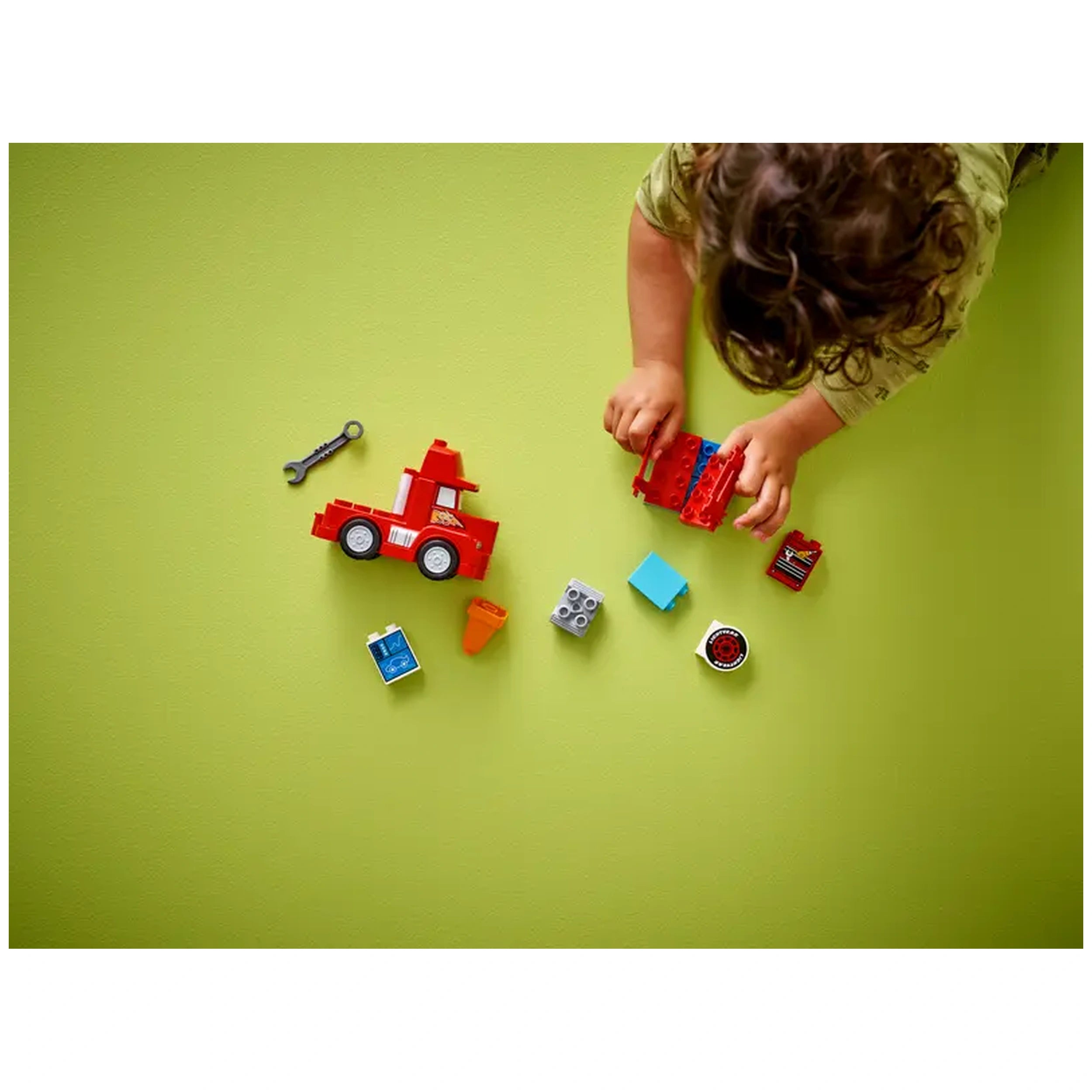 Child plays with a red LEGO® DUPLO® truck on a green surface, surrounded by colorful blocks and accessories for imaginative racing fun.