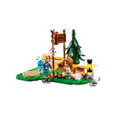 Two LEGO® Friends mini-dolls, Autumn and Nova, are at the Adventure Camp Archery Range, surrounded by trees and colorful playset elements. One doll holds a water bottle, while the other sits on the ground, aiming at an archery target. A playful raccoon figure is nearby, adding to the outdoor adventure atmosphere.