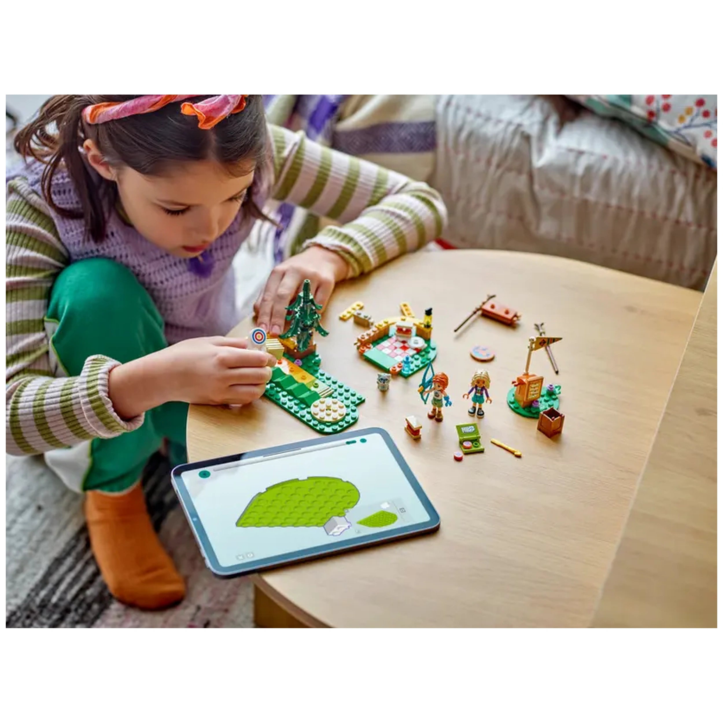 A child focusing intently on a colorful LEGO® Friends Adventure Camp set, adjusting a target while surrounded by mini-dolls and accessories.