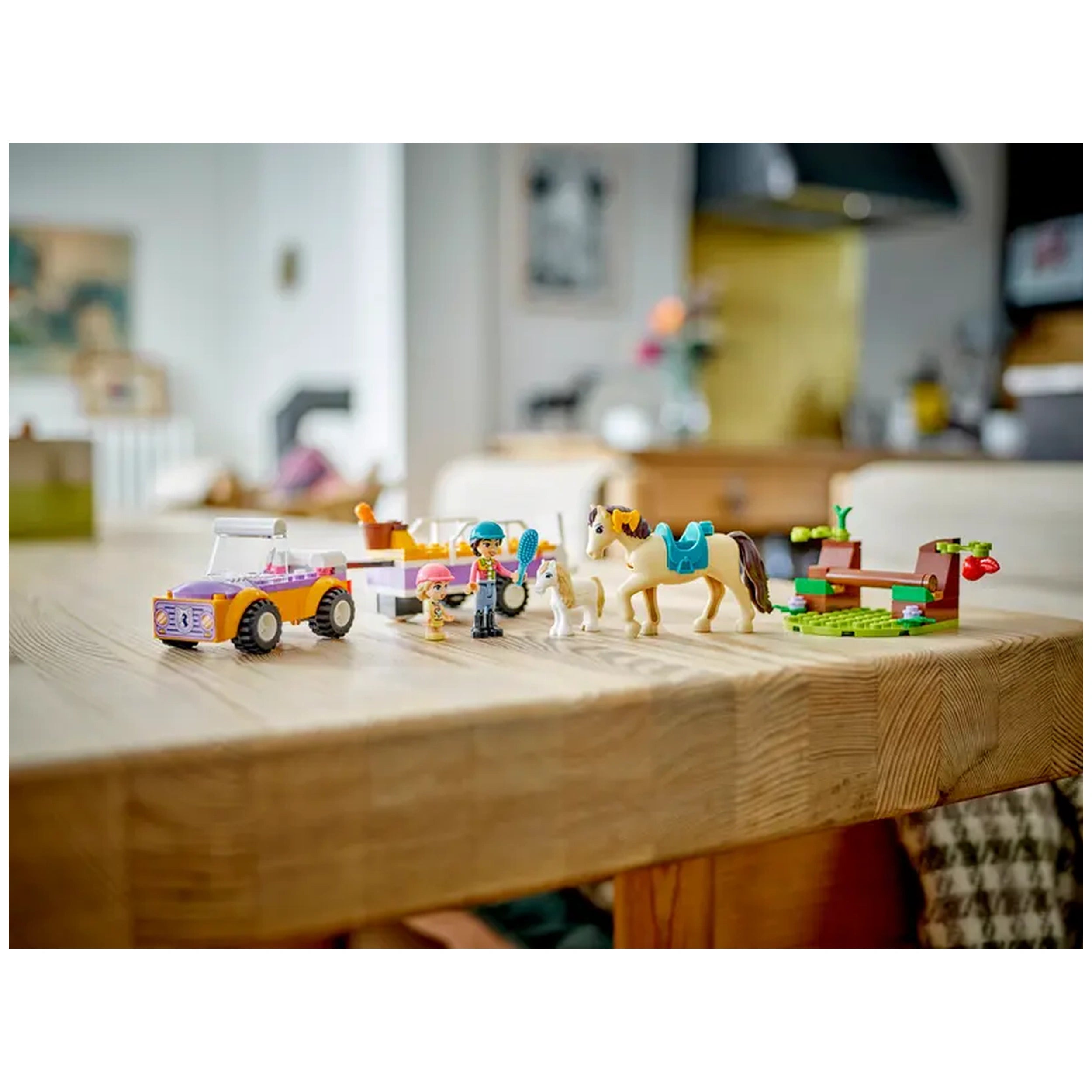 Colorful LEGO® Friends Horse and Pony Trailer set displayed on a wooden table, featuring a buildable car, two mini-figures, a horse, a pony, and a play area with a bench and apple tree.