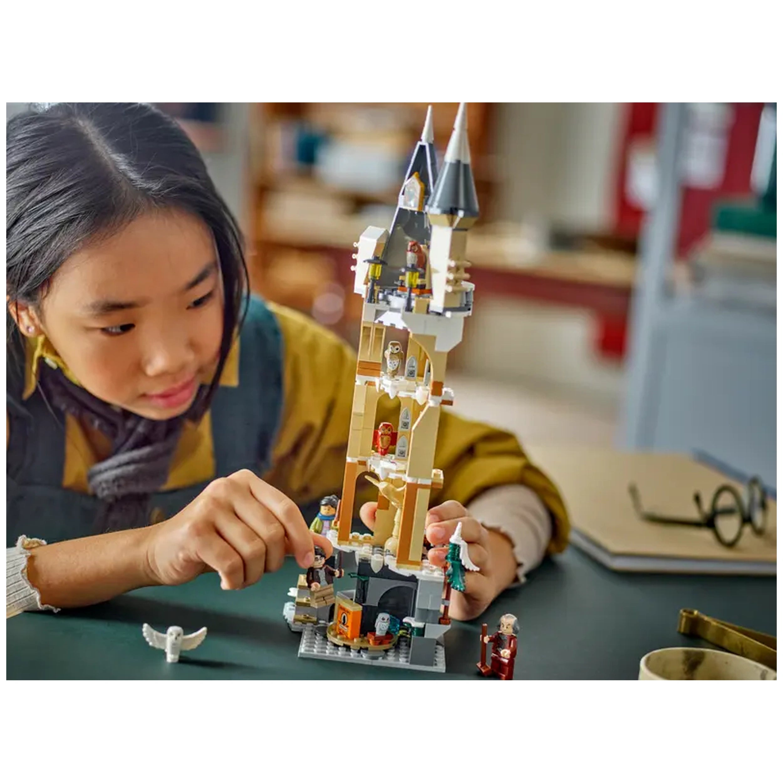 A young child carefully adjusts figures on the detailed Lego Harry Potter Hogwarts Castle Owlery construction set, featuring a tall tower with pointed roofs and owls.