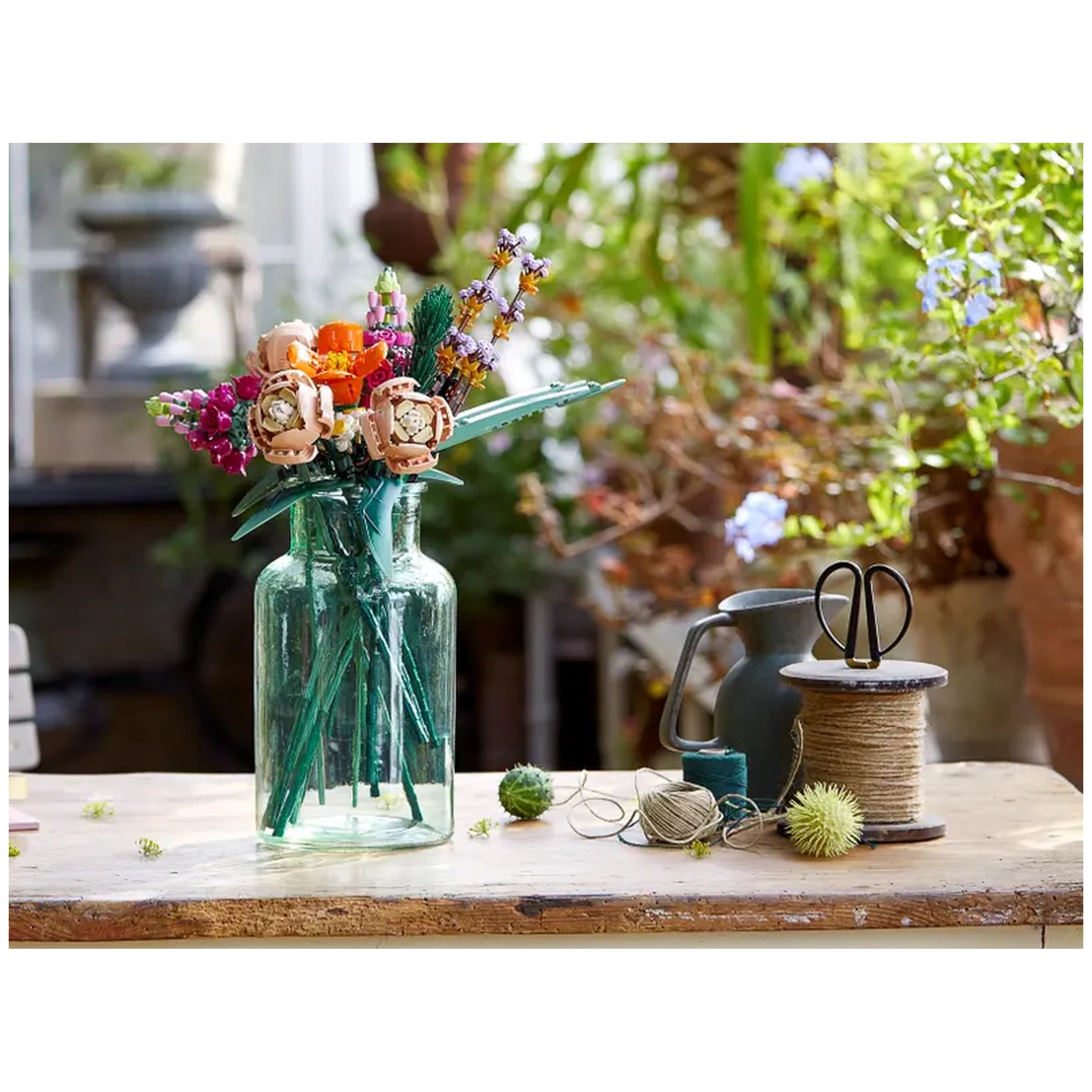 Colorful LEGO Flower Bouquet arranged in a green glass vase, surrounded by crafting tools and natural greenery on a wooden table.