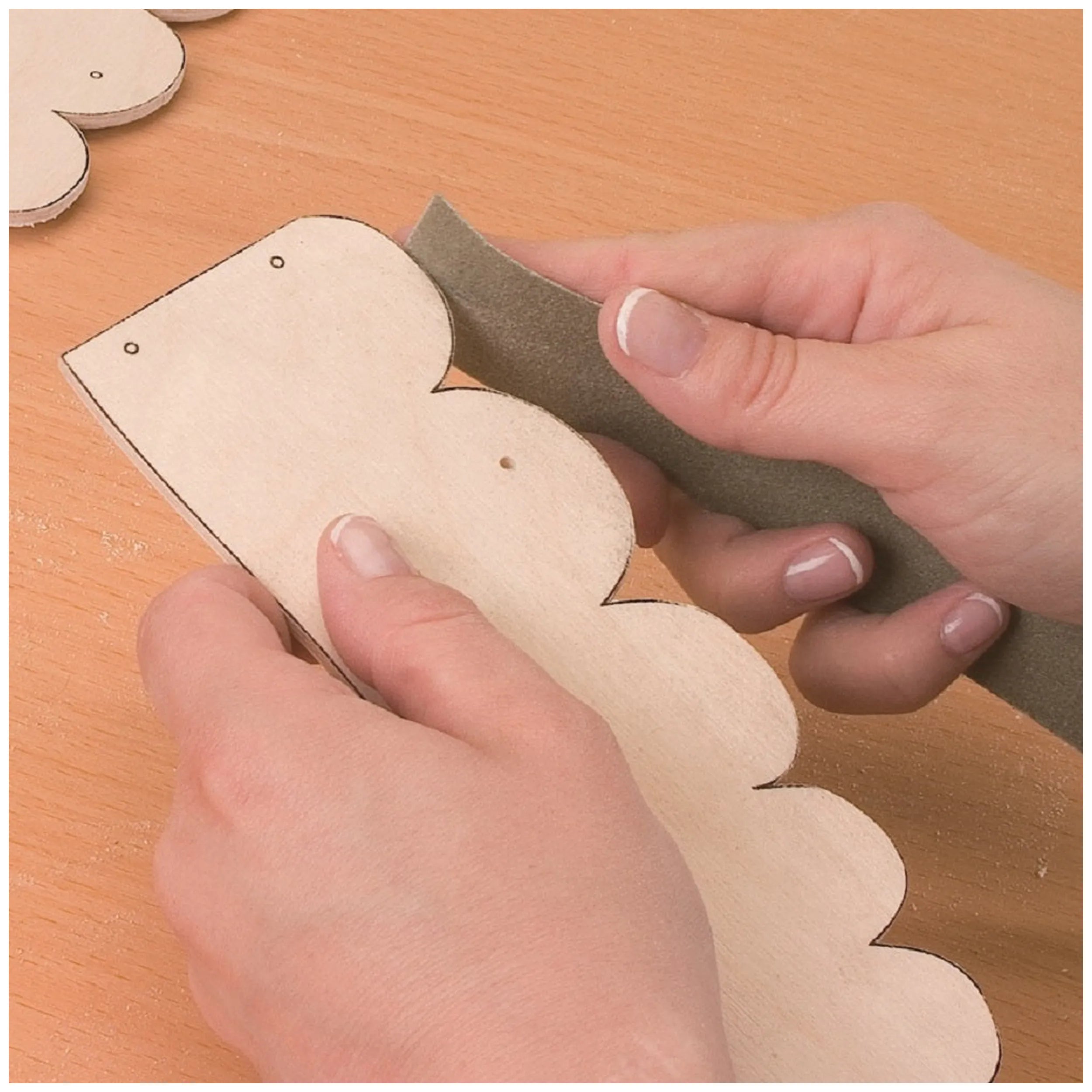 Hands sanding scalloped wooden piece, part of Prebaro Retwork Kit, on a wooden surface.