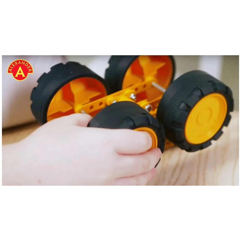 Child assembling Alexander Pro Muck Truck with black and orange wheels on a wooden surface.