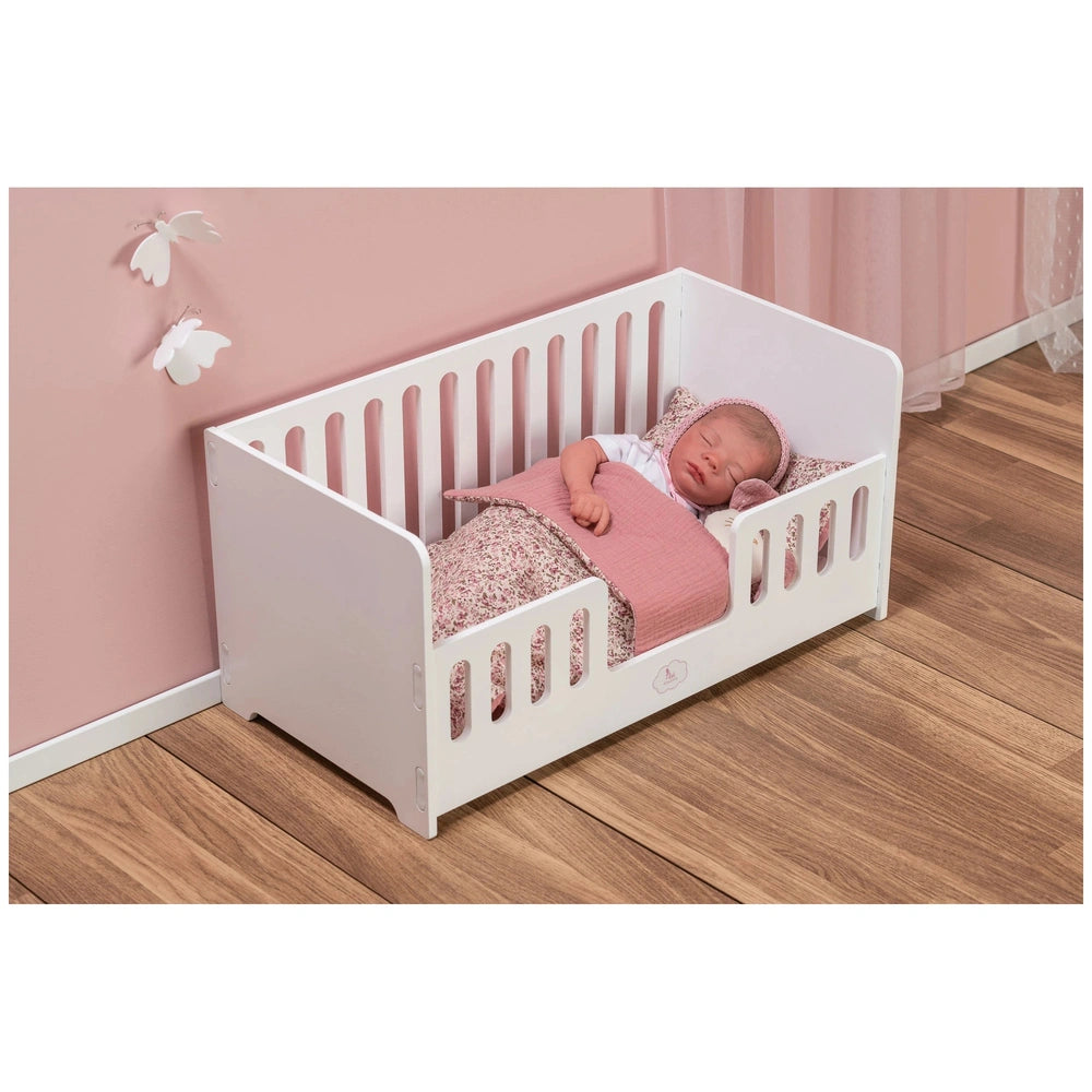 White wooden cradle with a sleeping doll, pink bedding, and floral patterns, set against a soft pink wall with butterfly decor.