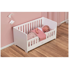 White wooden cradle with a sleeping doll, pink bedding, and floral patterns, set against a soft pink wall with butterfly decor.