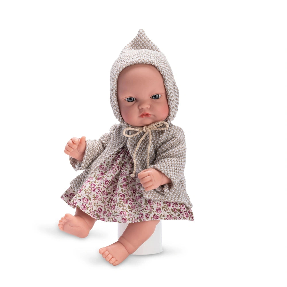 Bald doll in grey hooded cloak with patterned dress, sitting upright, showcasing flexible limbs and light-colored eyes.