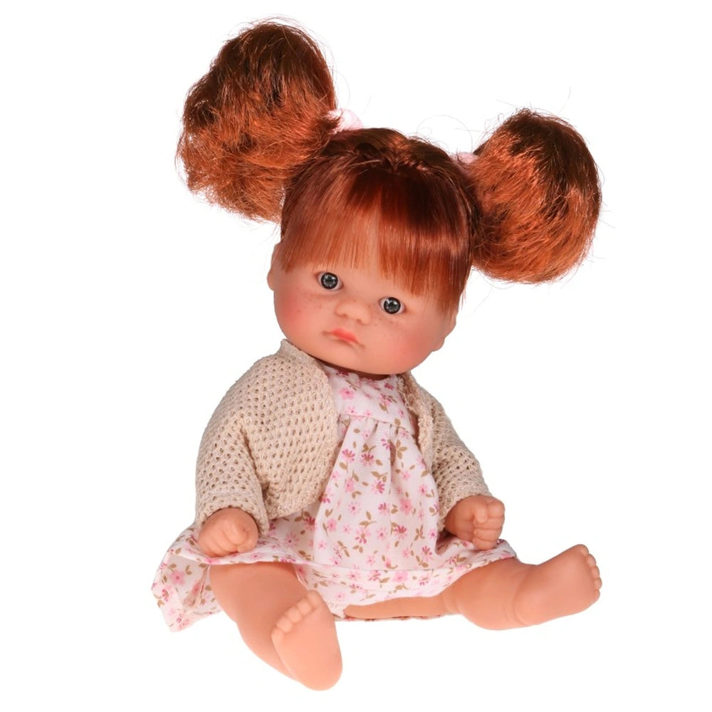 Laika doll with red hair in pigtails, wearing a pink floral dress and knitted cardigan, sitting with clenched fists.