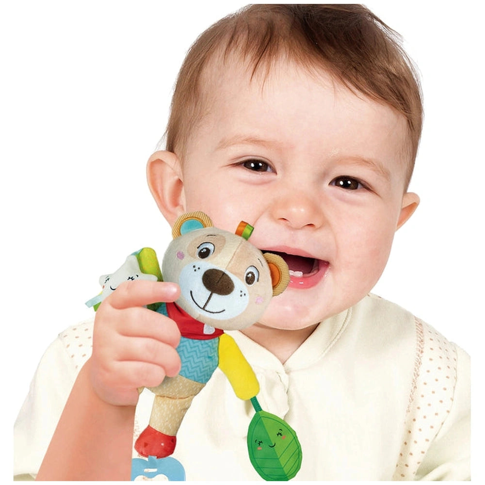 Baby Clementoni Easy-Peasy Soft Bear stuffed animal is held by a smiling child with light brown hair indoors.