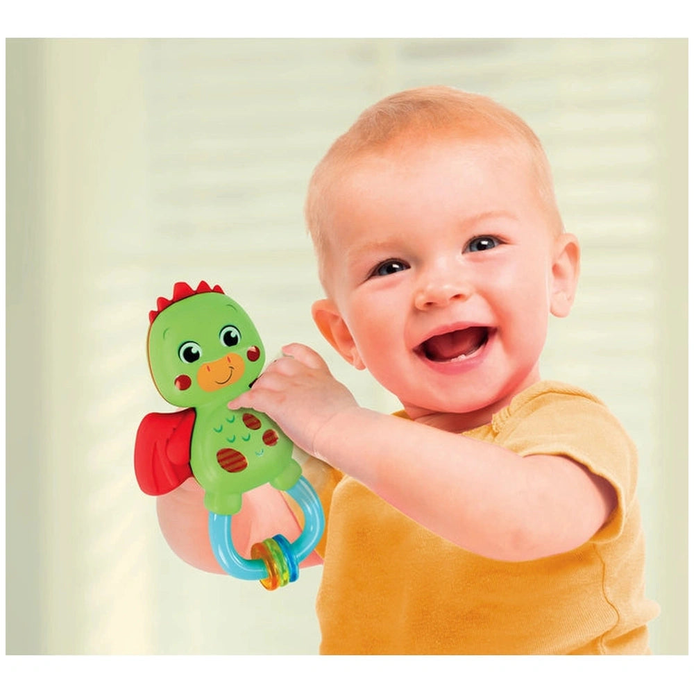 Baby Clementoni Little Dragon Rattle is held by a young child in a yellow top, featuring vibrant colors and a smiling face.