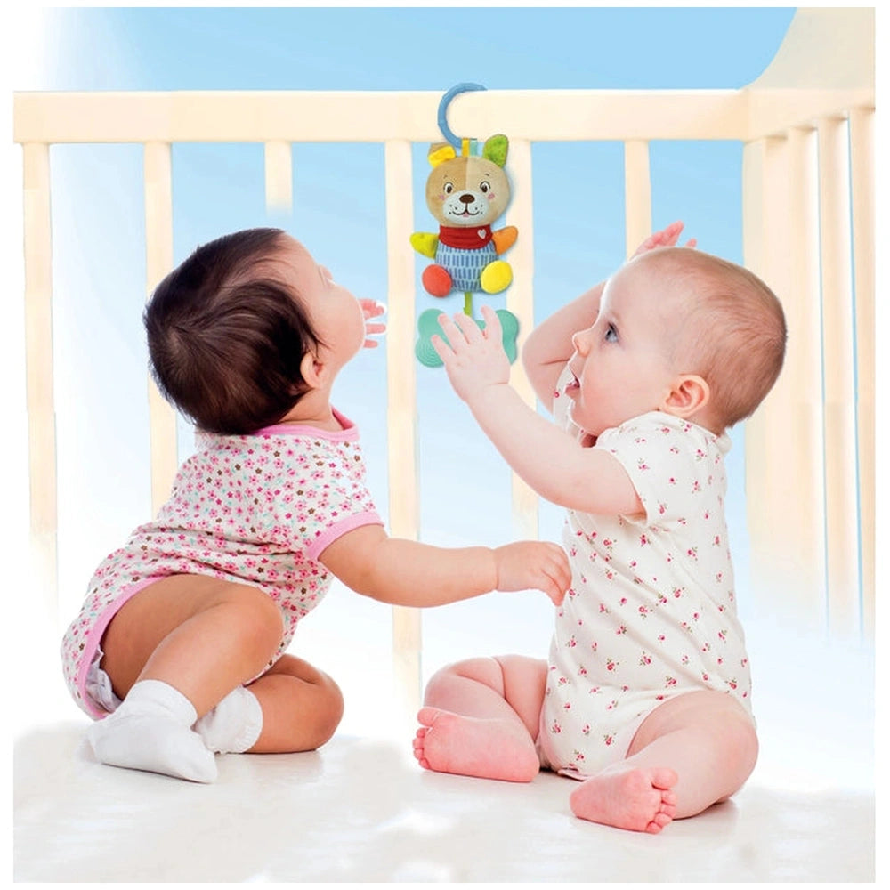 Baby Clementoni Lovely Soft Dog Rattle hangs above two infants in a calm, pastel-colored indoor setting.