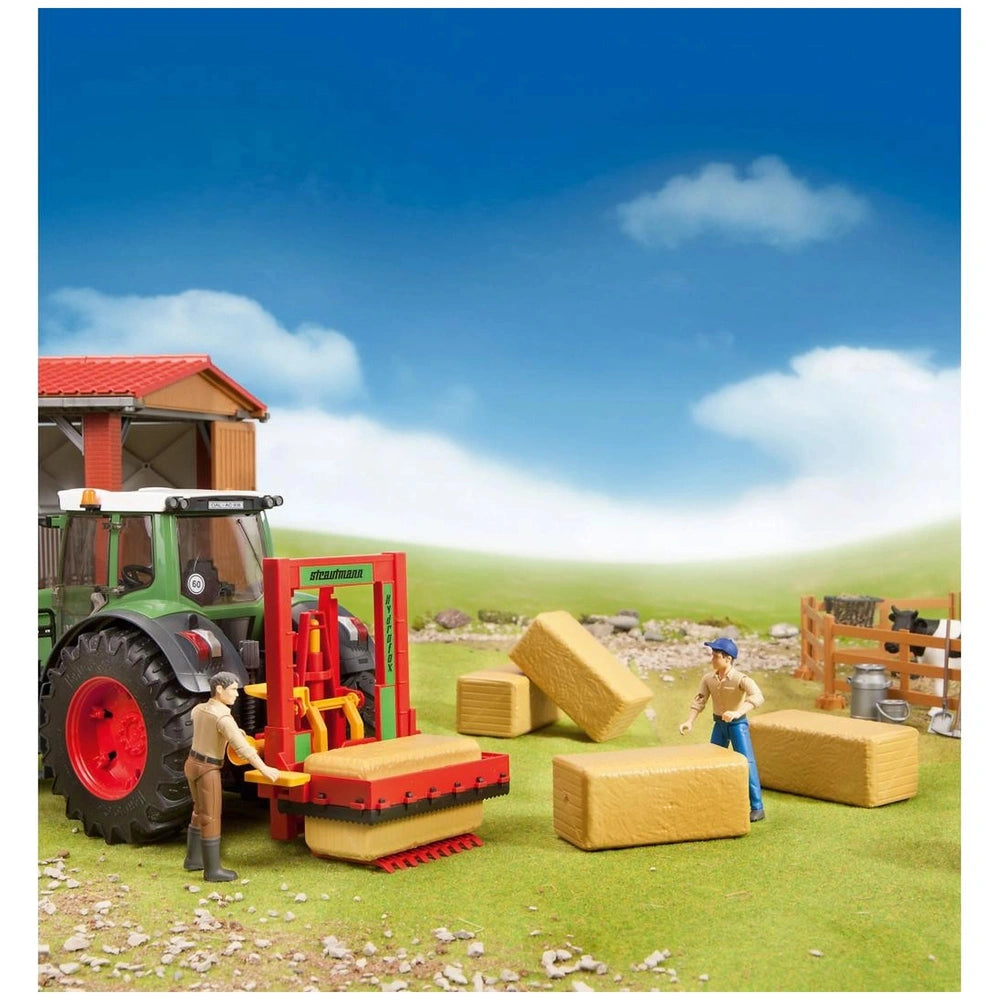 Toy farm scene with two figures moving four hay bales using a tractor attachment, cows in the background, under a clear sky.