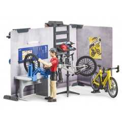 Toy bike shop playset with figurine fixing a bike, surrounded by tools, yellow bike, and poster on the wall.