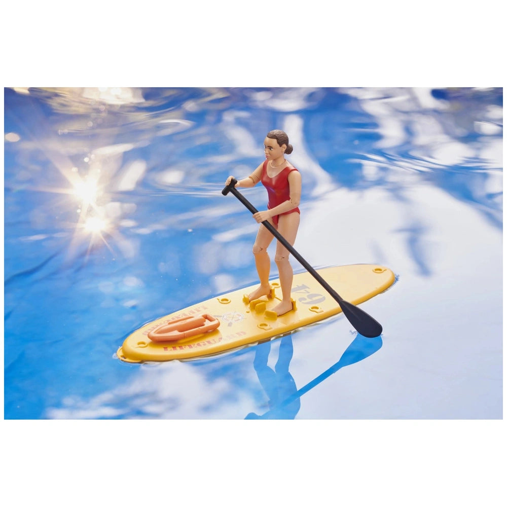 Lifeguard toy figure in red swimsuit on yellow stand-up paddleboard on blue water with lifebuoy.