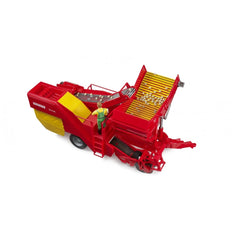Red and yellow Bruder Grimme potato digger toy with imitation potatoes on conveyor belt and a small farmer figure.