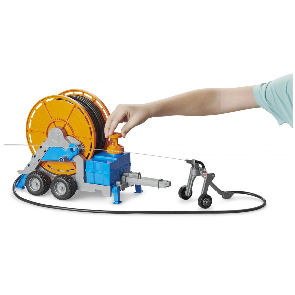 Hand cranking Bruder irrigation trailer with orange hose reel and detachable sprinkler, simulating farm equipment.