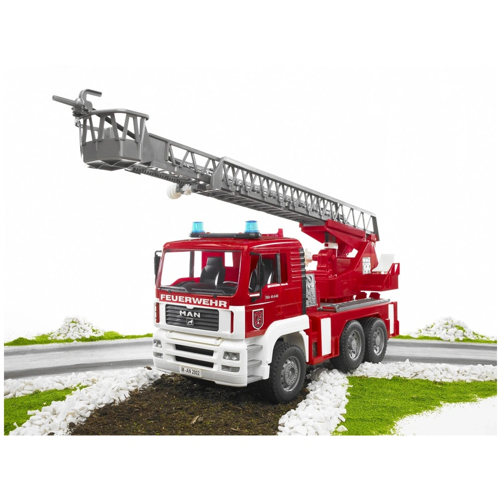 Red and white Bruder MAN TGA fire engine toy with blue lights and extended ladder on grassy, rocky terrain.
