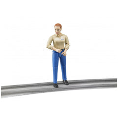 Bruder action figure with light skin, beige shirt, and blue trousers stands on a gray surface.