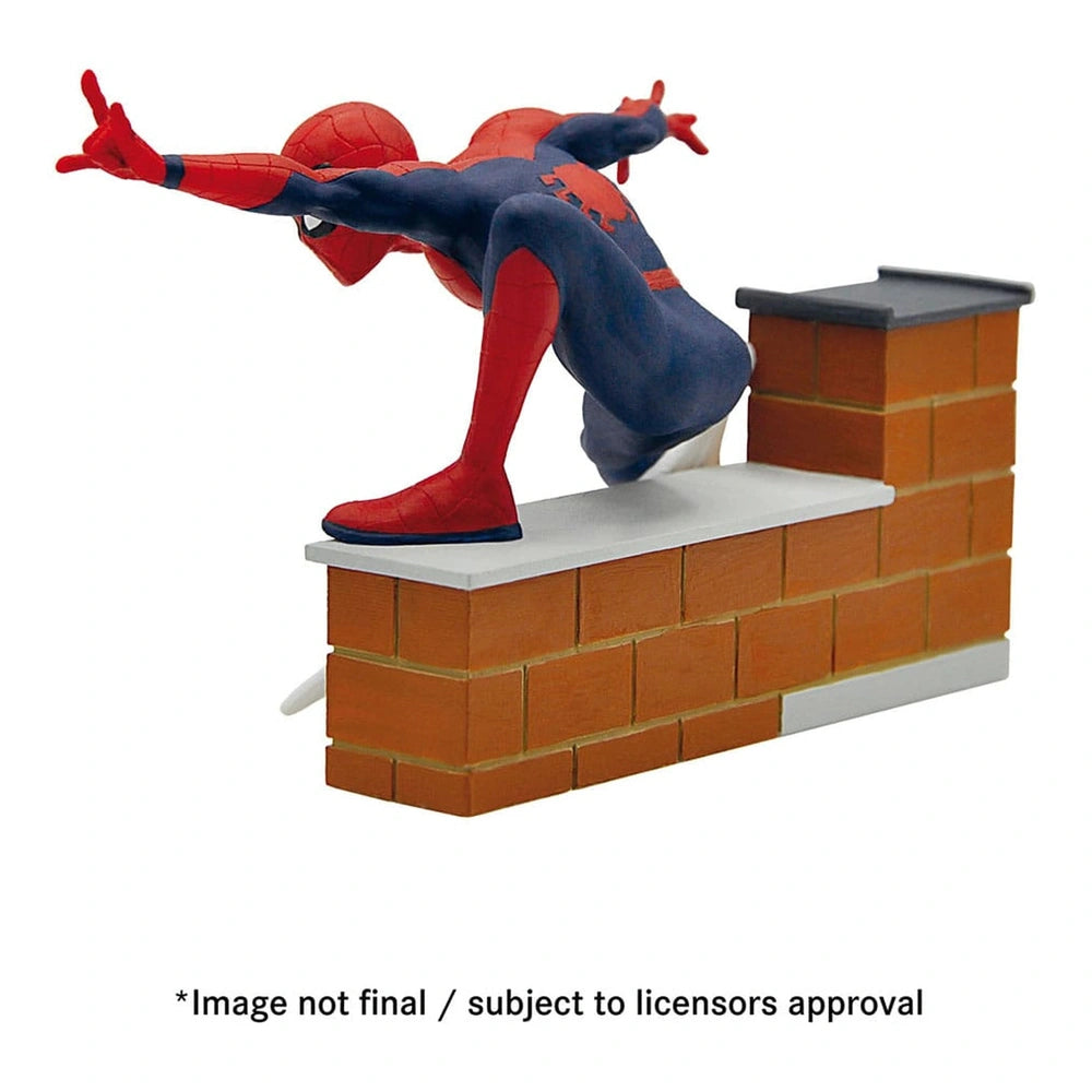 Spider-Man action figure in red and blue, dynamically posed on a white platform against a brick wall.