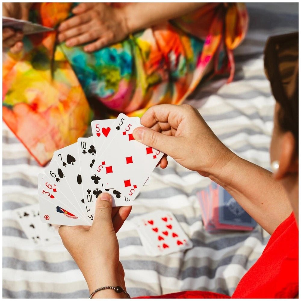 Dal Negro San Siro Pro Rummy Cards in blue-red deck held by hands against colorful fabric and a partially visible arm.