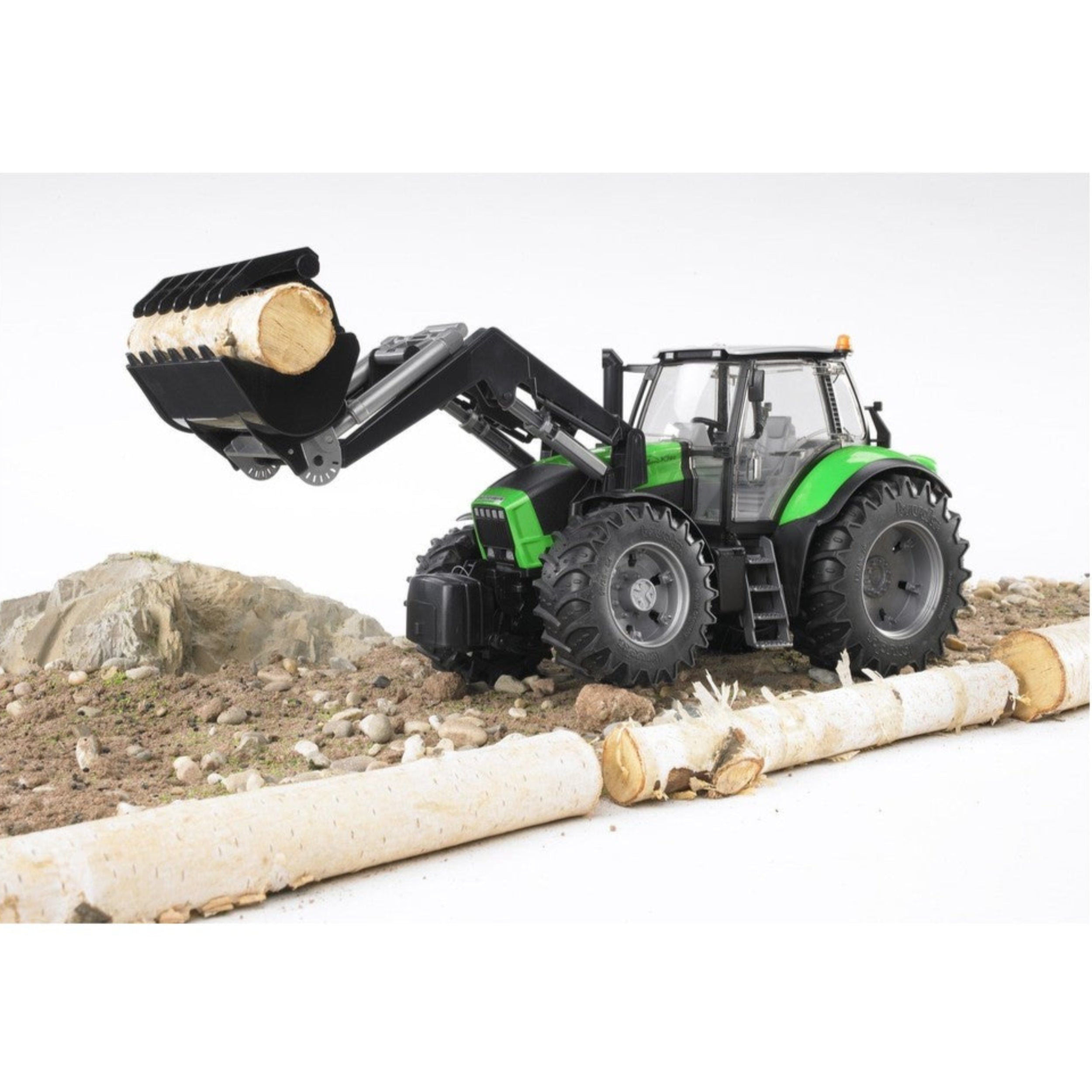 Bruder Deutz Agrotron X720 toy tractor with front loader lifting a log on rocky terrain.