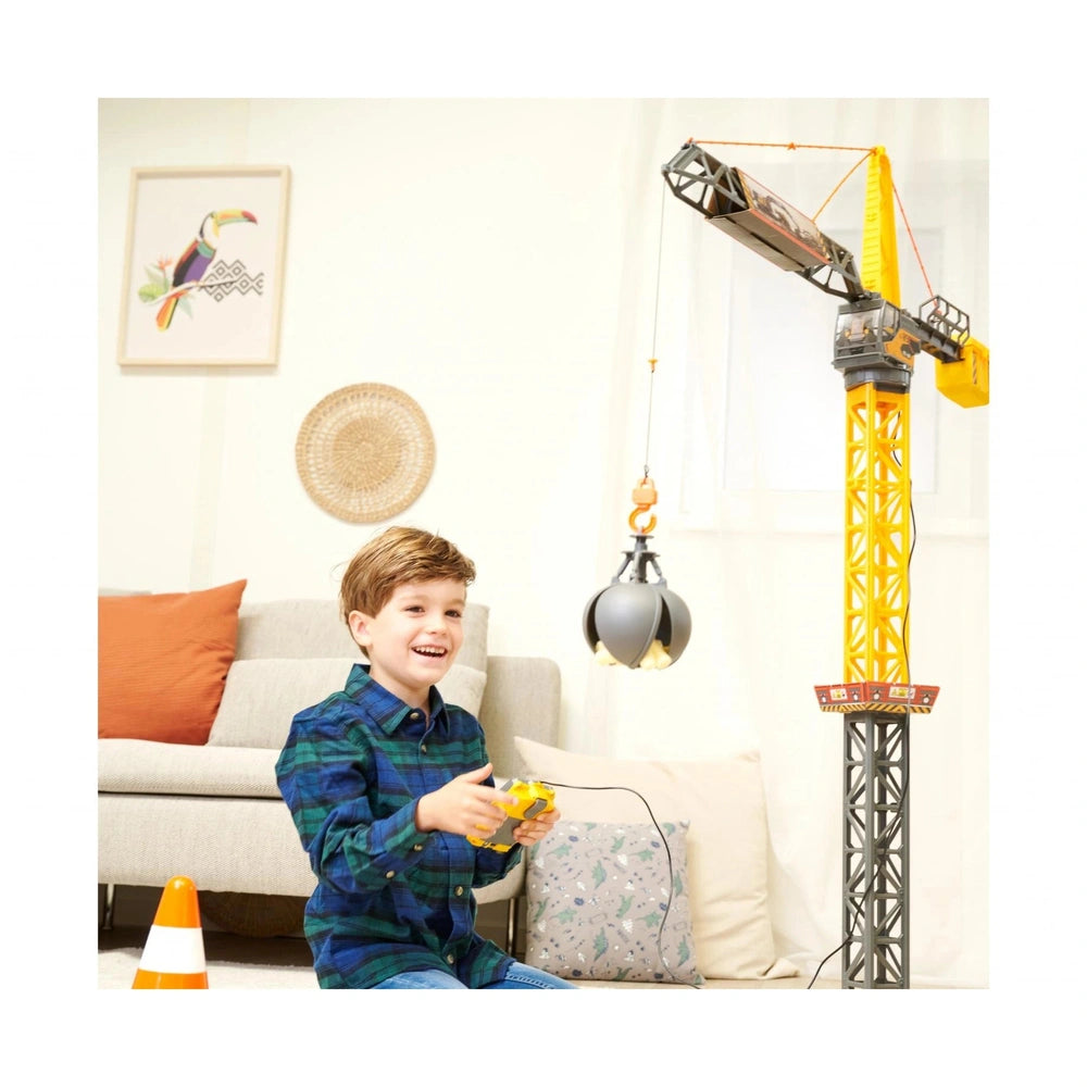 Mighty Crane play vehicle beside a young boy on a gray couch, featuring an orange pillow and black and gray balloons.