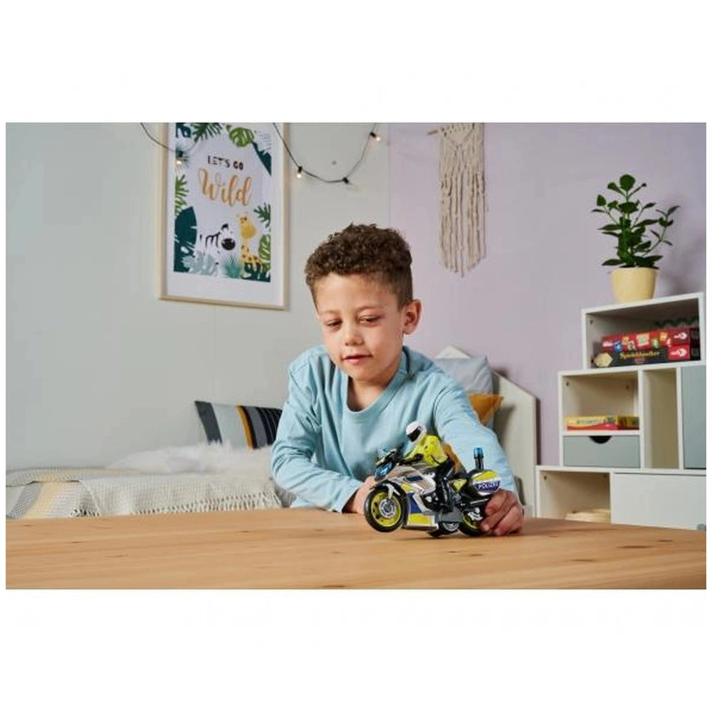 Dickie police motorbike toy with sounds and lights, played with by a young boy on a wooden table surrounded by colorful decor