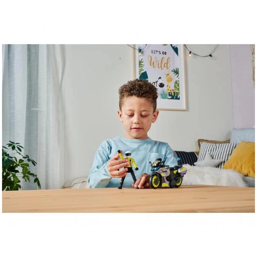 a couch, with a child in a blue shirt playing with a yellow and black Dickie police motorbike in a cozy living room.
