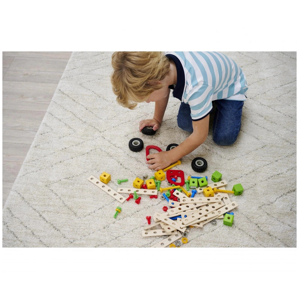 Eichhorn construction set with 111 plastic parts and wheels, as a child with blonde hair plays on a light brown wooden floor.