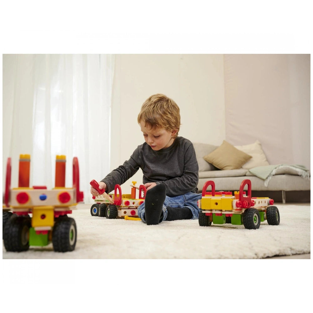 Eichhorn Constructor Truck set with a child playing on a white rug, holding a toy vehicle with red and yellow wheels.