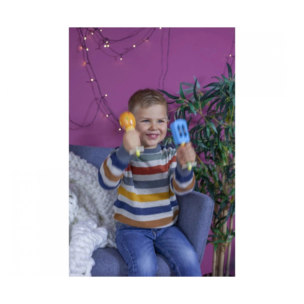 Eichhorn maracas held by a smiling child on a blue couch, surrounded by a cheerful indoor setting.