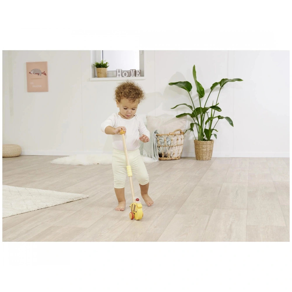 Eichhorn Push Bee toy in childs hands, set in a minimalist room with white walls and a potted plant in the background.