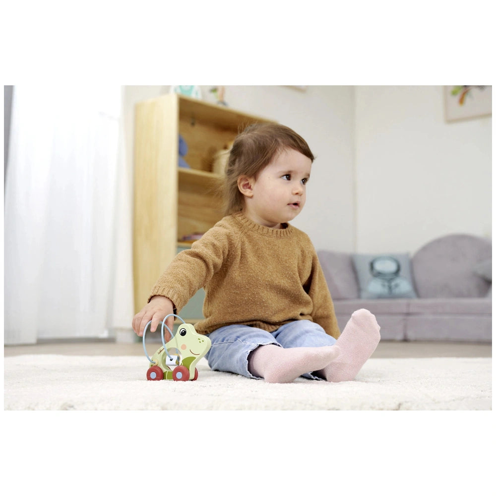 Eichhorn Push Frog activity toy with a child in a cozy living room, holding the green wheeled toy on a white carpet.