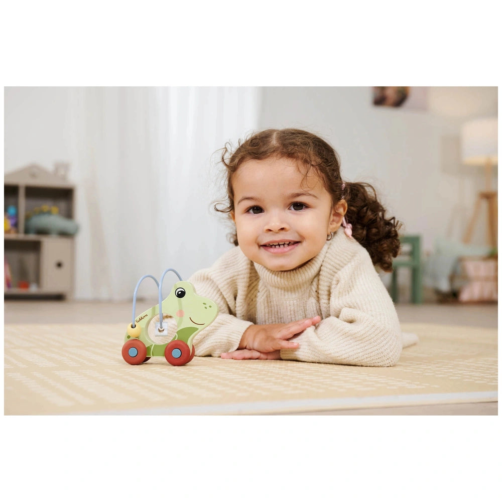 Eichhorn Push Frog Baby Activity Toy with a smiling child playing on a beige carpet in a cozy indoor setting.