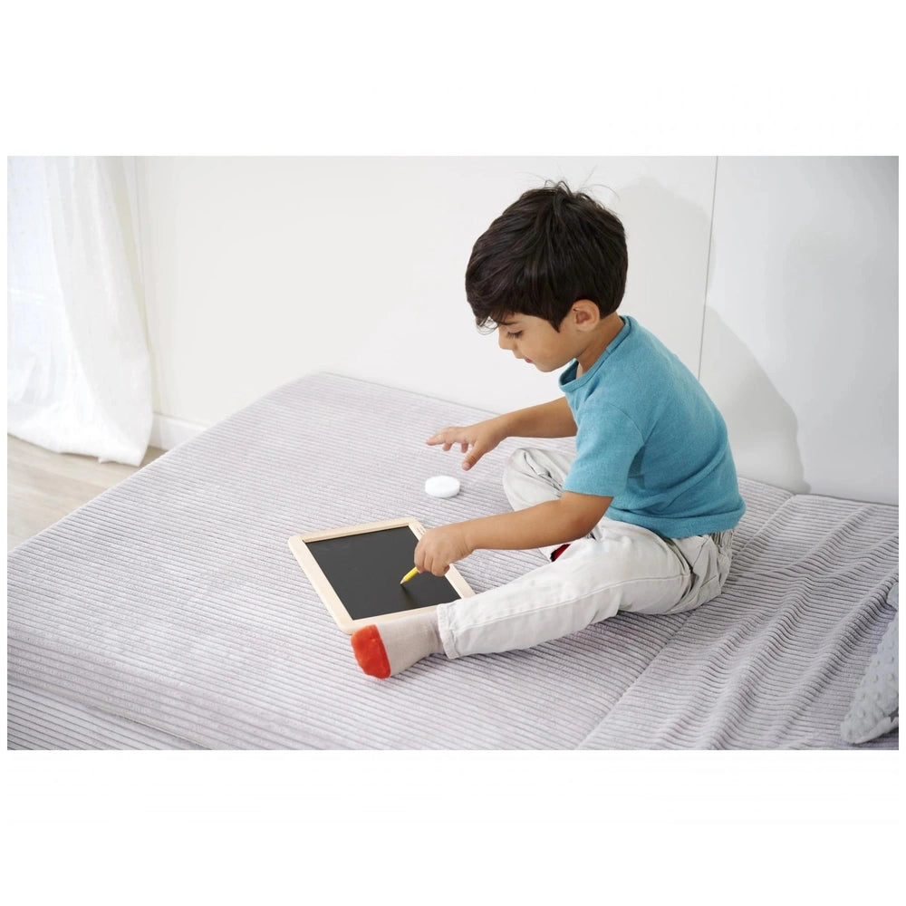Eichhorn Small Blackboard - Child engaged in creative play with tablet and stylus, sitting on a bed in a bright room.