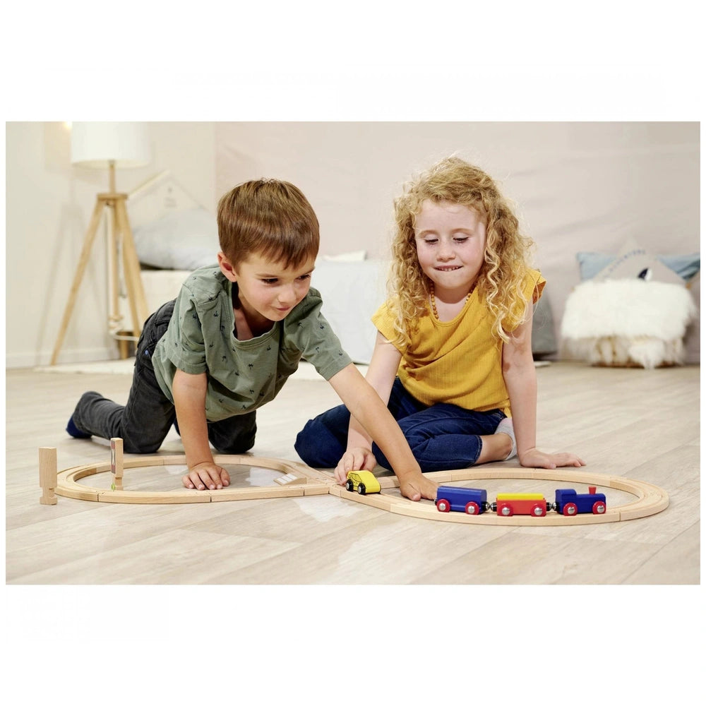 Eichhorn Train Track Playset features two children playing with colorful wooden trains on a minimalistic room floor.