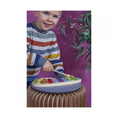 Eichhorn Xylophone in use by a smiling child, striking colorful keys with a mallet against a purple wall background.