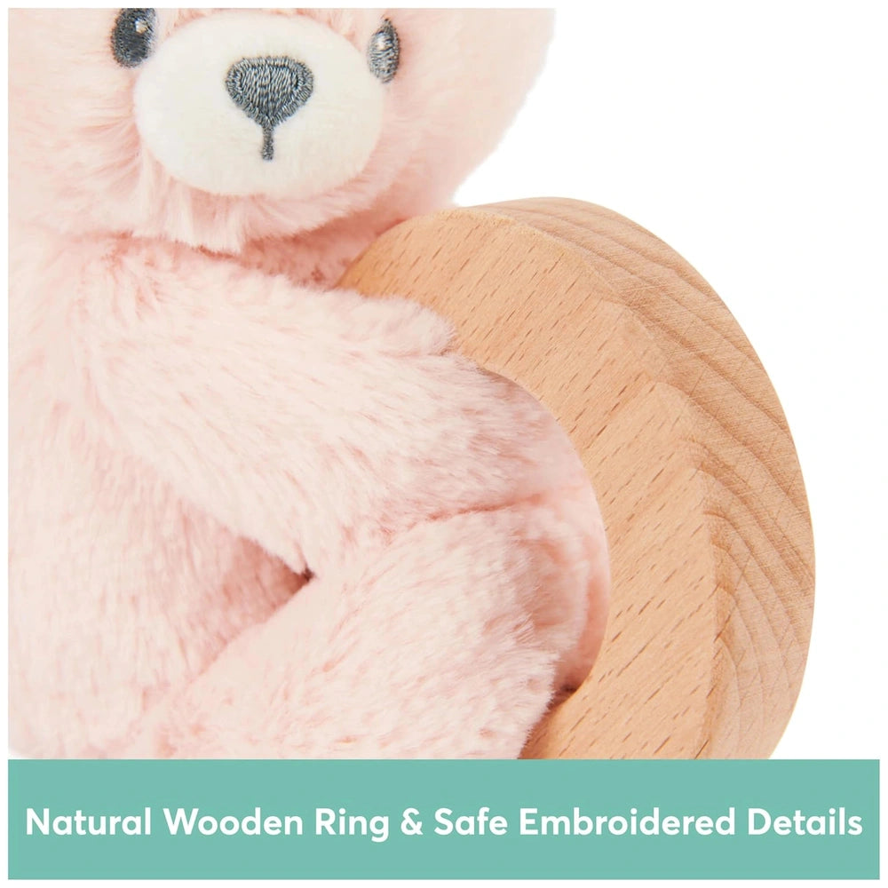Pink teddy bear holding a light-colored wooden ring with safe embroidered details, featuring a white snout and black eyes.
