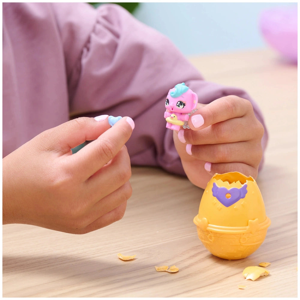 Hatchimals Alive mini figure in pink and blue held by a person with light pink nails next to a yellow egg on a wooden surface