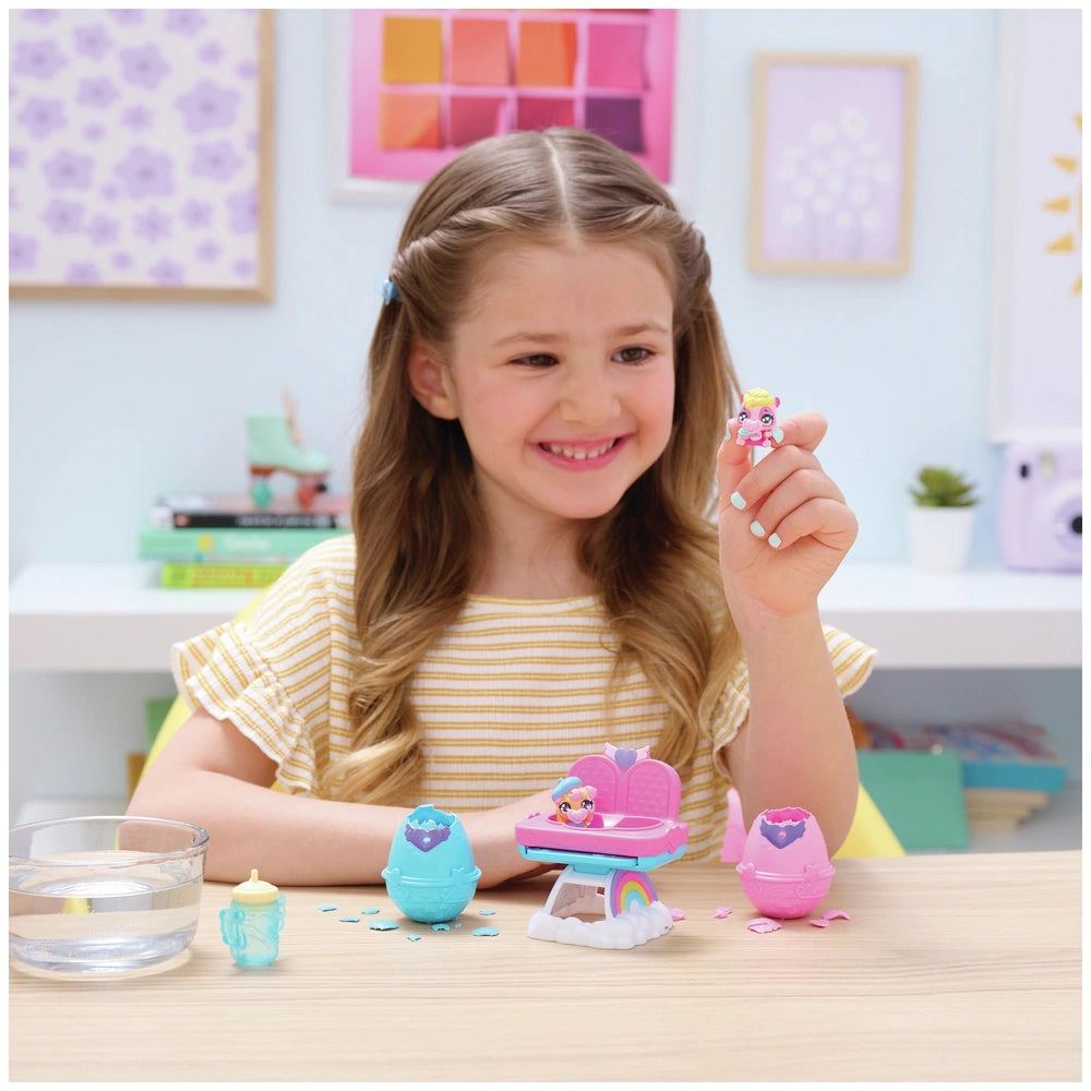 Hatchimals Alive playset featuring a smiling girl in a yellow top holding a toy egg at a colorful table filled with toys.